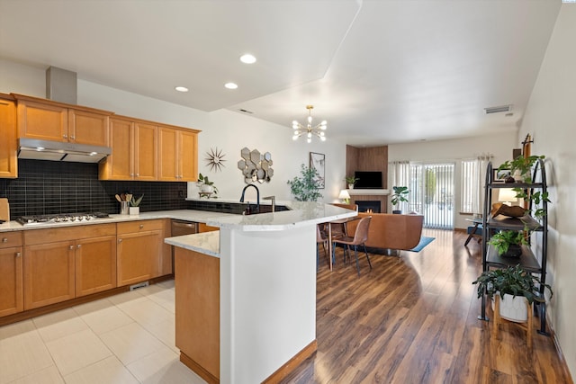 kitchen featuring stainless steel gas stovetop, decorative backsplash, light stone counters, kitchen peninsula, and light wood-type flooring