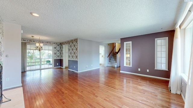 unfurnished living room with baseboards, a textured ceiling, a notable chandelier, and stairway