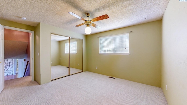 unfurnished bedroom with carpet floors, a textured ceiling, a ceiling fan, visible vents, and a closet