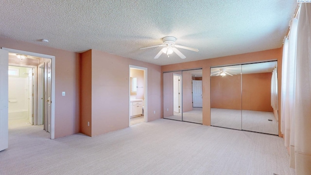 unfurnished bedroom featuring carpet floors, a textured ceiling, multiple closets, and ensuite bath
