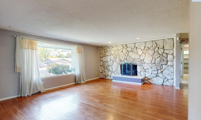 unfurnished living room with a textured ceiling, a stone fireplace, baseboards, and hardwood / wood-style floors