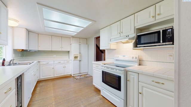 kitchen with backsplash, light wood-type flooring, white cabinets, under cabinet range hood, and white appliances