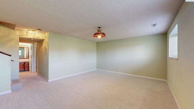 spare room with a textured ceiling, baseboards, light colored carpet, and visible vents