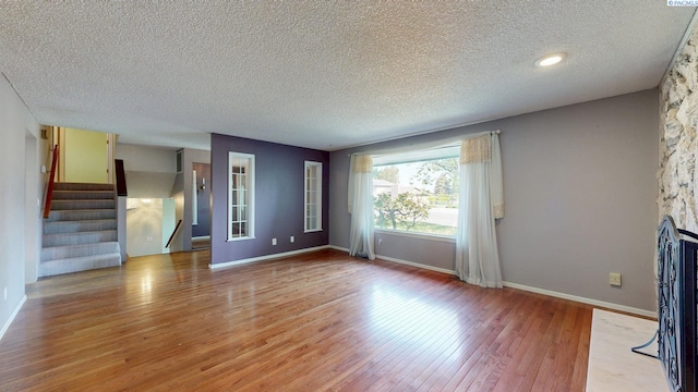 unfurnished living room featuring baseboards, a textured ceiling, light wood finished floors, and stairway