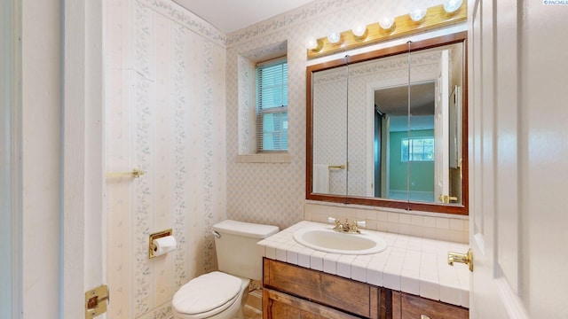 half bathroom with toilet, wallpapered walls, and vanity