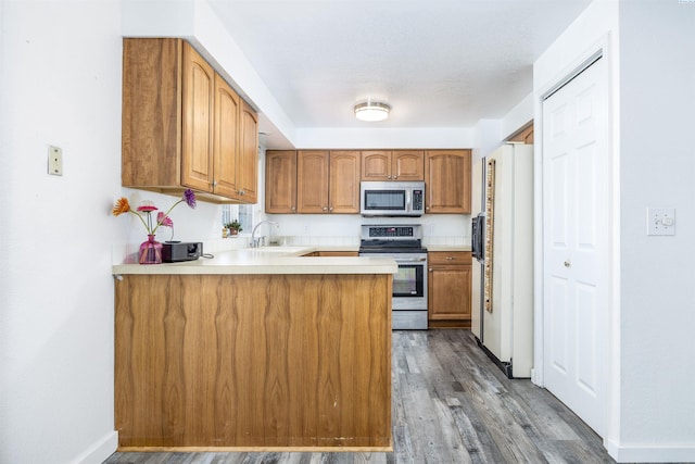 706 W 42nd Ave, Kennewick, WA 99337 - kitchen with appliances with stainless steel finishes, brown cabinets, a peninsula, dark wood-style flooring, and a sink