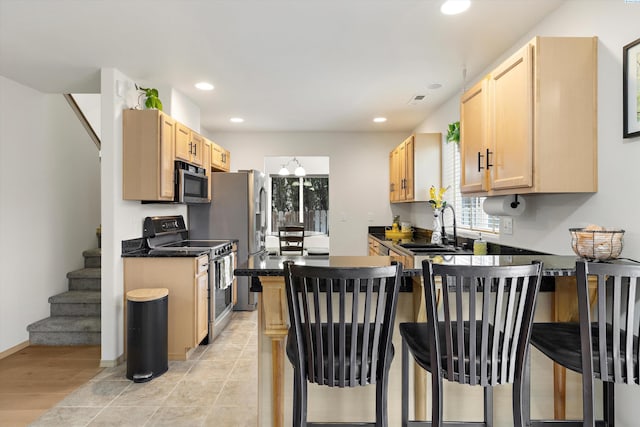 kitchen with a peninsula, a sink, appliances with stainless steel finishes, dark countertops, and a kitchen bar