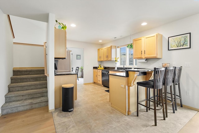 kitchen featuring dark countertops, black dishwasher, a breakfast bar area, and light brown cabinetry