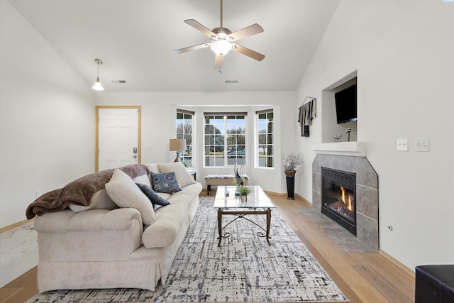 living room with ceiling fan, visible vents, light wood-style floors, vaulted ceiling, and a tiled fireplace