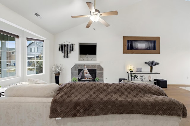 bedroom featuring a tile fireplace, wood finished floors, visible vents, a ceiling fan, and vaulted ceiling