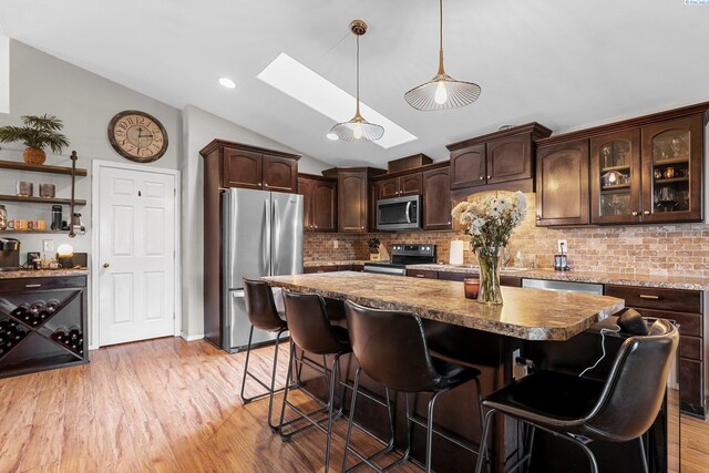 5504 Koufax Ln, Pasco, WA 99301 - kitchen with appliances with stainless steel finishes, a skylight, dark brown cabinetry, lofted ceiling, and a breakfast bar area