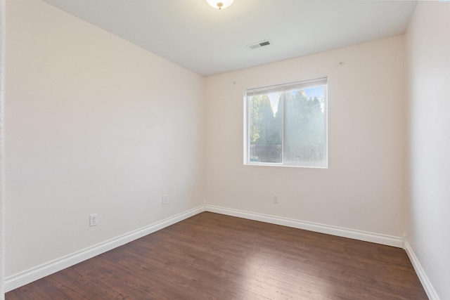 empty room featuring dark wood-style floors, visible vents, and baseboards