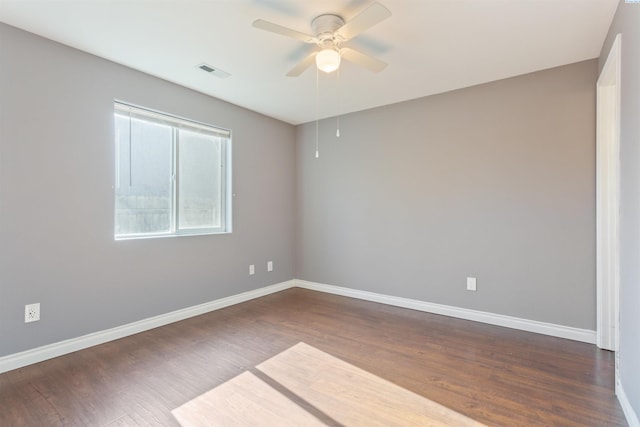 spare room with dark wood-style flooring, visible vents, and baseboards