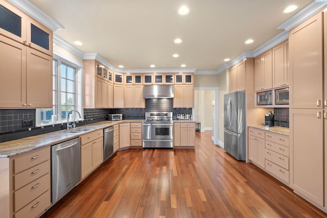 kitchen featuring dark wood-style flooring, a sink, ornamental molding, stainless steel appliances, and under cabinet range hood