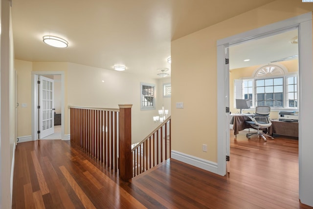 hall with an upstairs landing, baseboards, and wood finished floors