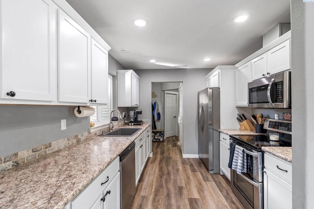 kitchen with sink, white cabinetry, stainless steel appliances, light stone counters, and wood-type flooring