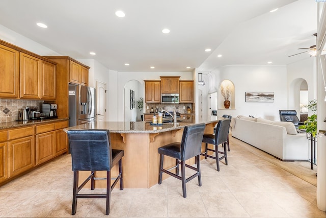 439 Cherry Blossom Loop, Richland, WA 99352 - kitchen featuring stainless steel appliances, arched walkways, brown cabinetry, decorative backsplash, and a breakfast bar
