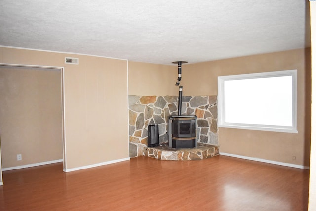 unfurnished living room featuring a wood stove, hardwood / wood-style flooring, and a textured ceiling