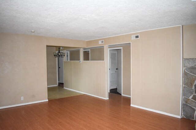 unfurnished room featuring an inviting chandelier, a textured ceiling, and hardwood / wood-style floors