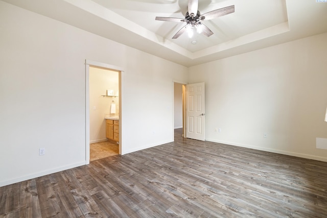 unfurnished bedroom with wood finished floors, a ceiling fan, baseboards, a raised ceiling, and ensuite bath