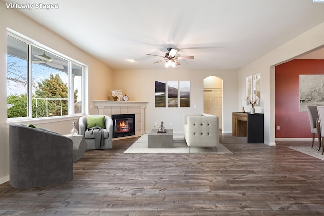 interior space featuring arched walkways, wood finished floors, a ceiling fan, baseboards, and a tiled fireplace