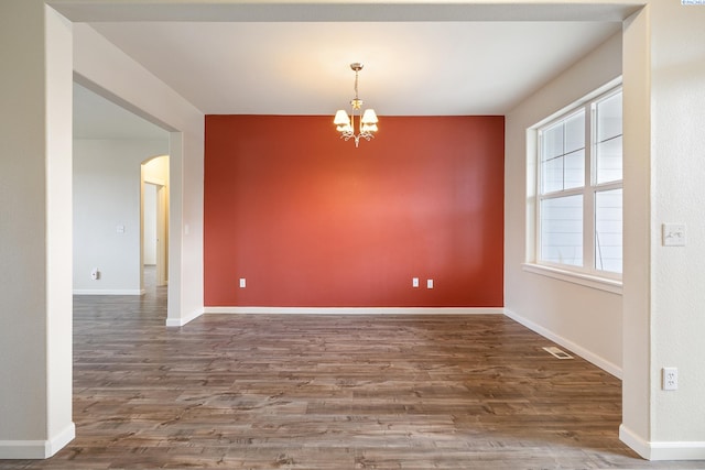 empty room with arched walkways, a notable chandelier, baseboards, and wood finished floors