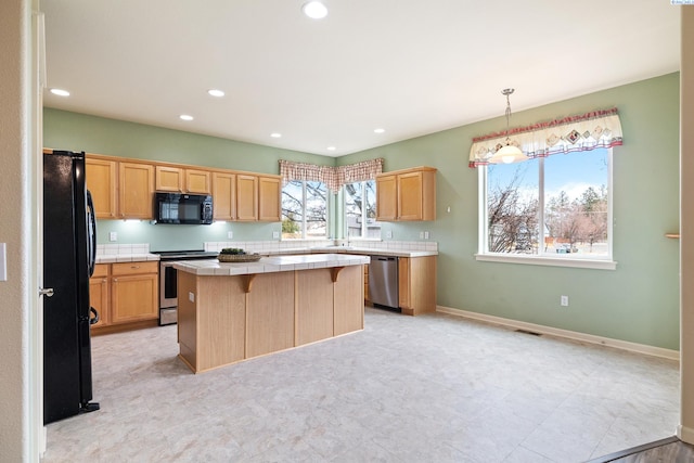 kitchen featuring baseboards, tile countertops, a kitchen island, black appliances, and a wealth of natural light