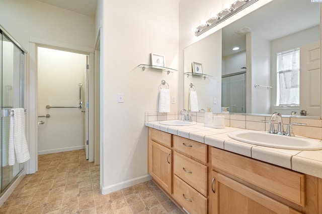 bathroom with double vanity, a stall shower, a sink, and baseboards