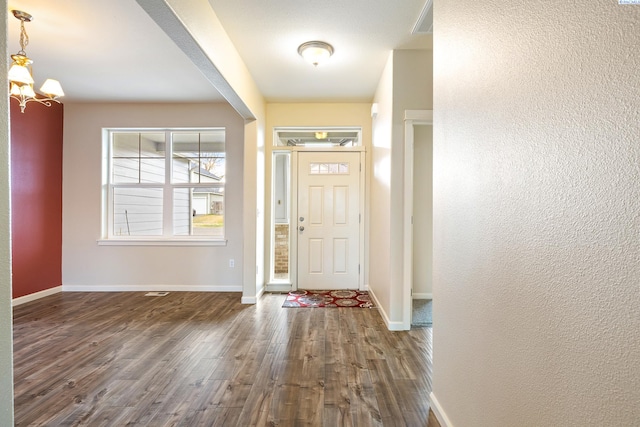 foyer entrance featuring a notable chandelier, baseboards, and dark wood-type flooring