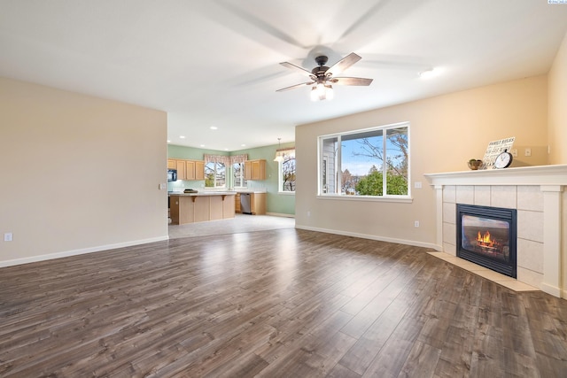 unfurnished living room featuring ceiling fan, a fireplace, baseboards, and wood finished floors