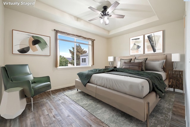 bedroom featuring a ceiling fan, a tray ceiling, baseboards, and wood finished floors