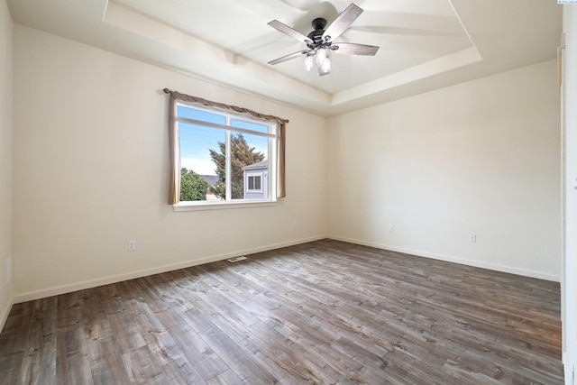 spare room with ceiling fan, a tray ceiling, wood finished floors, and baseboards