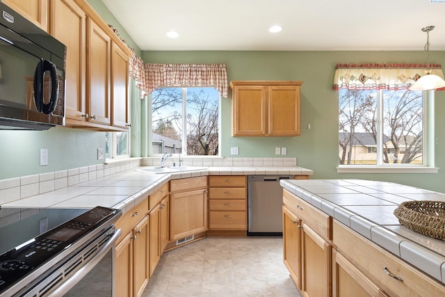 kitchen with tile countertops, appliances with stainless steel finishes, light brown cabinets, pendant lighting, and a sink