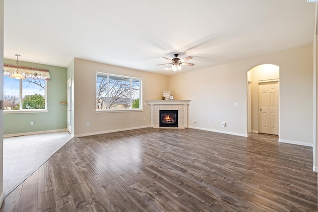 unfurnished living room with baseboards, a fireplace, arched walkways, and dark wood finished floors