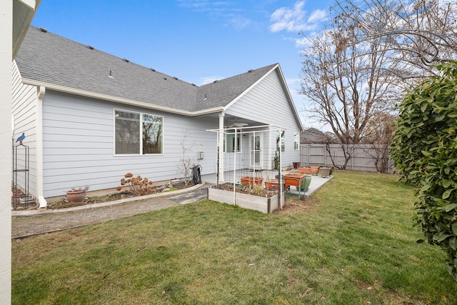 back of property featuring a shingled roof, a vegetable garden, fence, and a lawn