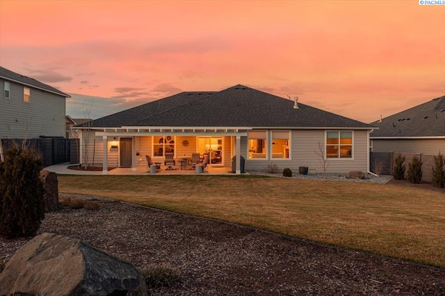 back of house at dusk with a patio, a lawn, and a fenced backyard