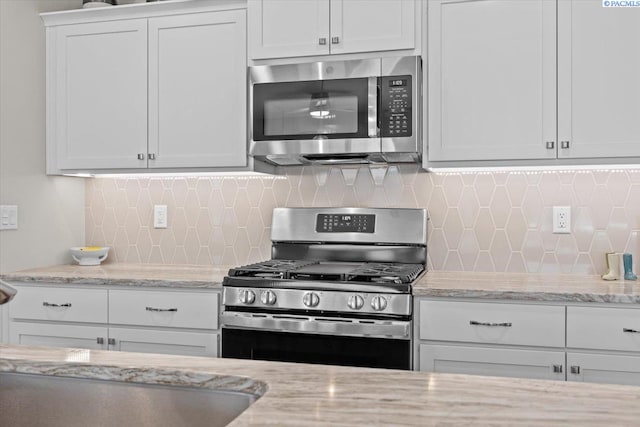 kitchen with light stone countertops, white cabinetry, stainless steel appliances, and decorative backsplash