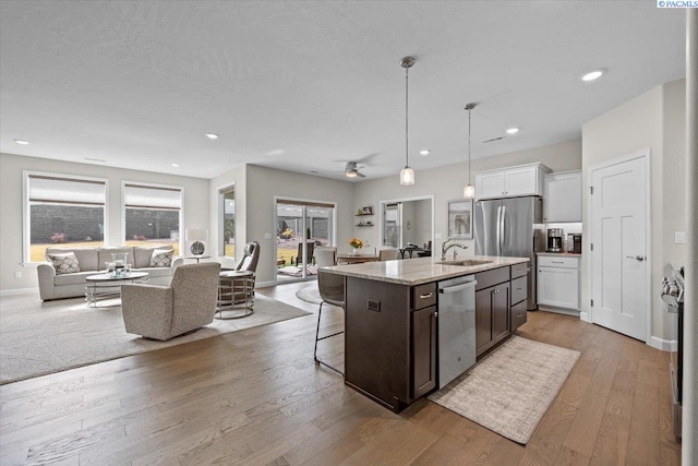 kitchen with a breakfast bar area, stainless steel appliances, a sink, open floor plan, and light wood finished floors