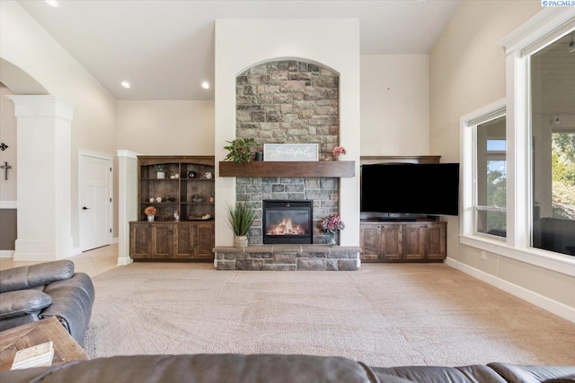 living room with decorative columns, a stone fireplace, a towering ceiling, and light colored carpet