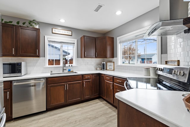 kitchen featuring a sink, visible vents, light countertops, appliances with stainless steel finishes, and wall chimney range hood