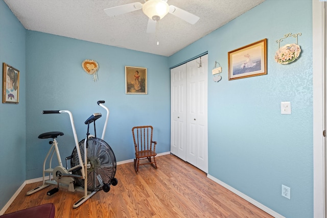 workout area with ceiling fan, wood-type flooring, and a textured ceiling