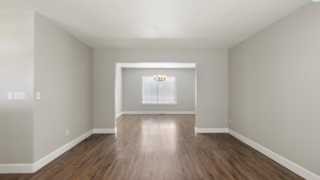 empty room featuring a chandelier, dark wood-style flooring, and baseboards