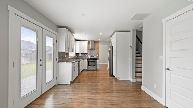 kitchen featuring appliances with stainless steel finishes, wall chimney range hood, tasteful backsplash, light wood finished floors, and recessed lighting
