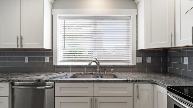 kitchen with stainless steel dishwasher, a sink, white cabinetry, decorative backsplash, and dark stone countertops