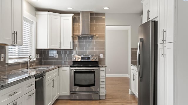 kitchen featuring stainless steel appliances, wall chimney exhaust hood, a sink, white cabinets, and recessed lighting