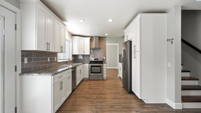 kitchen with appliances with stainless steel finishes, wall chimney exhaust hood, a sink, dark wood-style floors, and decorative backsplash