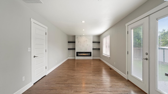 unfurnished living room with plenty of natural light, french doors, wood finished floors, recessed lighting, and a large fireplace
