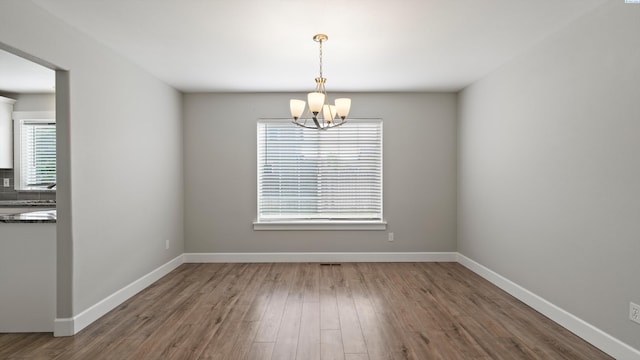 unfurnished room featuring a chandelier, wood finished floors, and baseboards