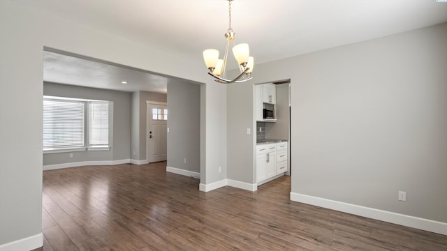 empty room featuring a chandelier, dark wood-style floors, and baseboards