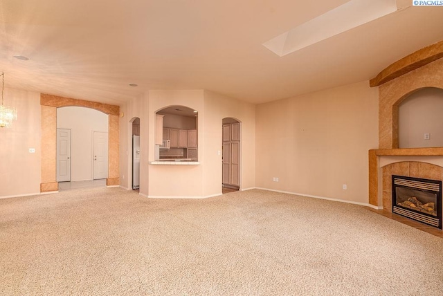 unfurnished living room with arched walkways, a tile fireplace, carpet flooring, and baseboards